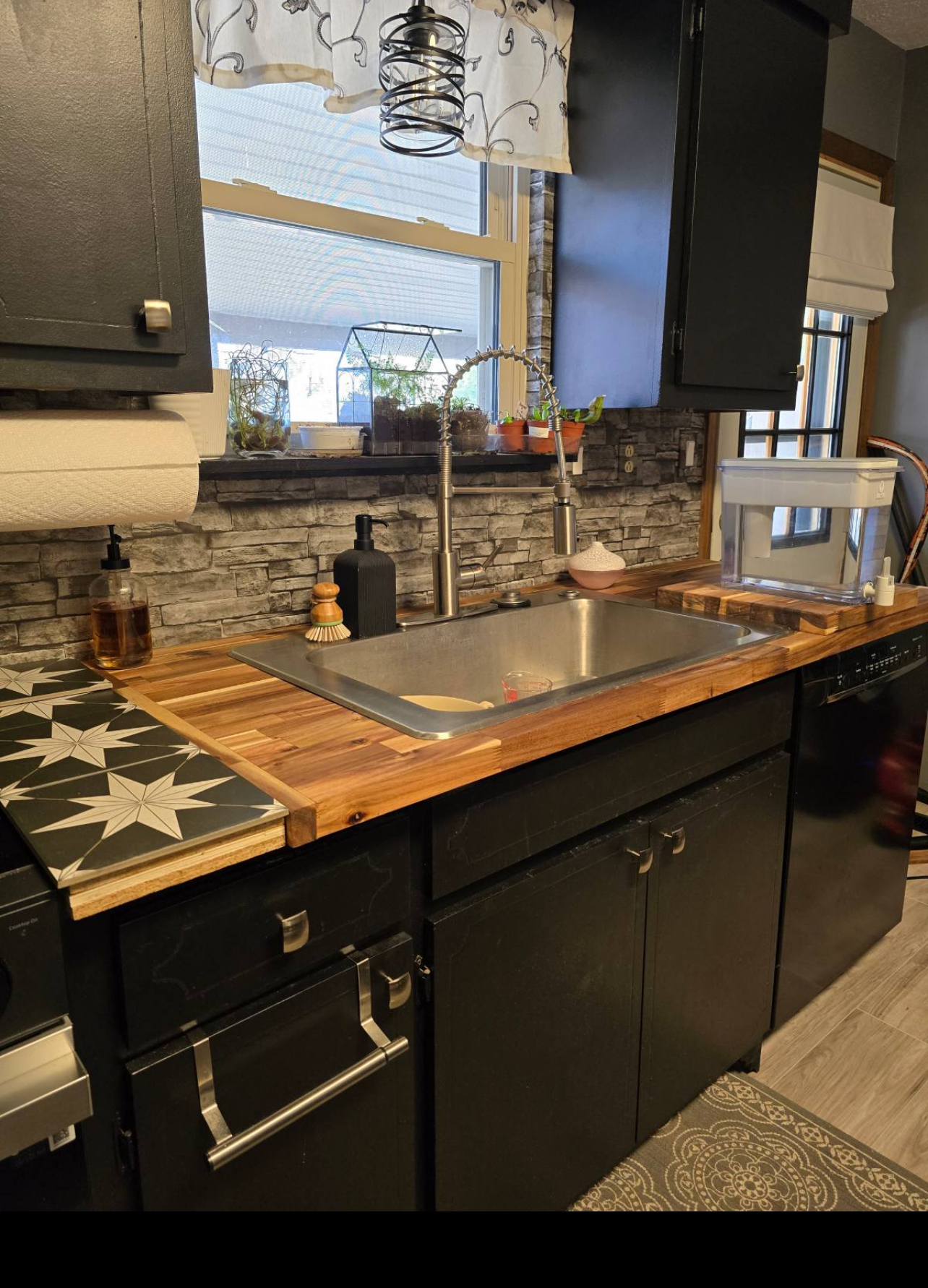 Dark kitchen sink run with butcher block countertop and stone backsplash